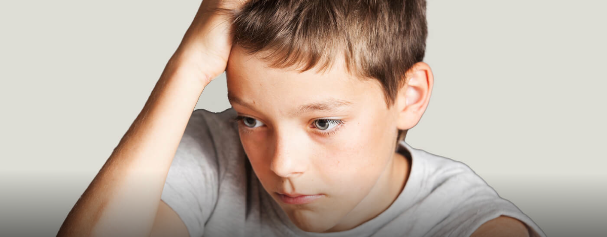 Child with short brown hair resting his head on one hand and looking down with a sad expression