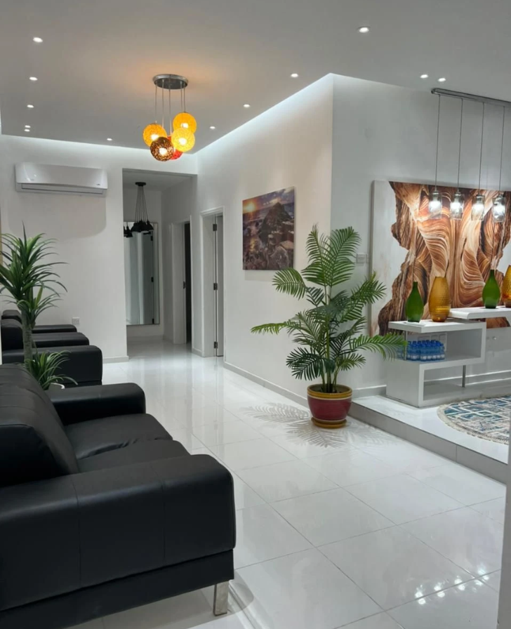 Waiting area with black leather sofas, a potted palm and orange globe pendant lights over a white tiled floor