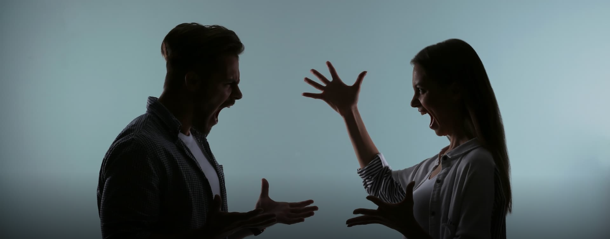 Silhouettes of a man and a woman facing each other and shouting with their hands raised in an argument