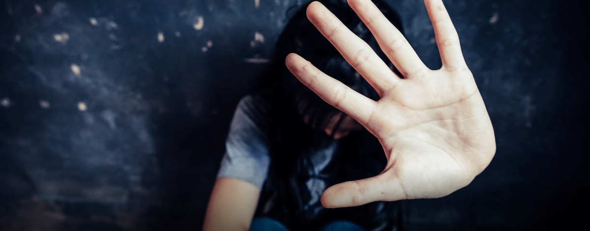 Person sitting against a dark wall behind an outstretched open hand held toward the camera in a stop gesture