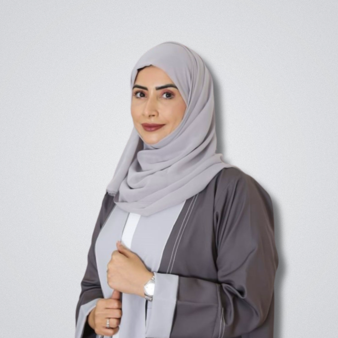 Woman in a light grey hijab and dark grey abaya, smiling slightly and holding the front of her abaya