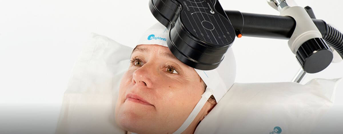 Woman lying on a pillow in a MagVenture cap with a TMS coil positioned over her head
