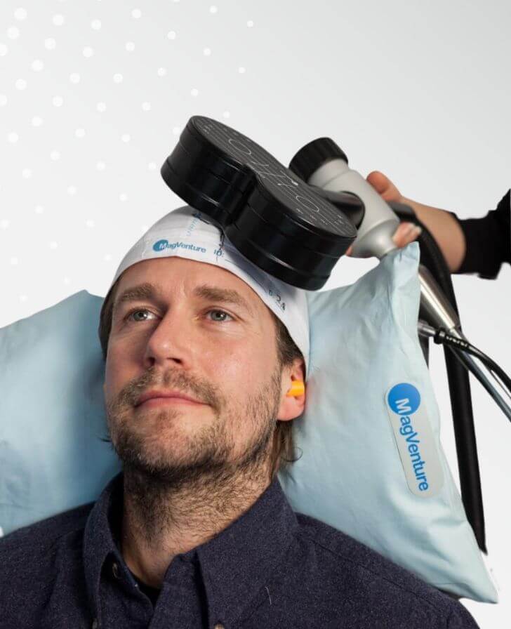 Man resting on a pillow in a MagVenture cap while a TMS coil is held against his head