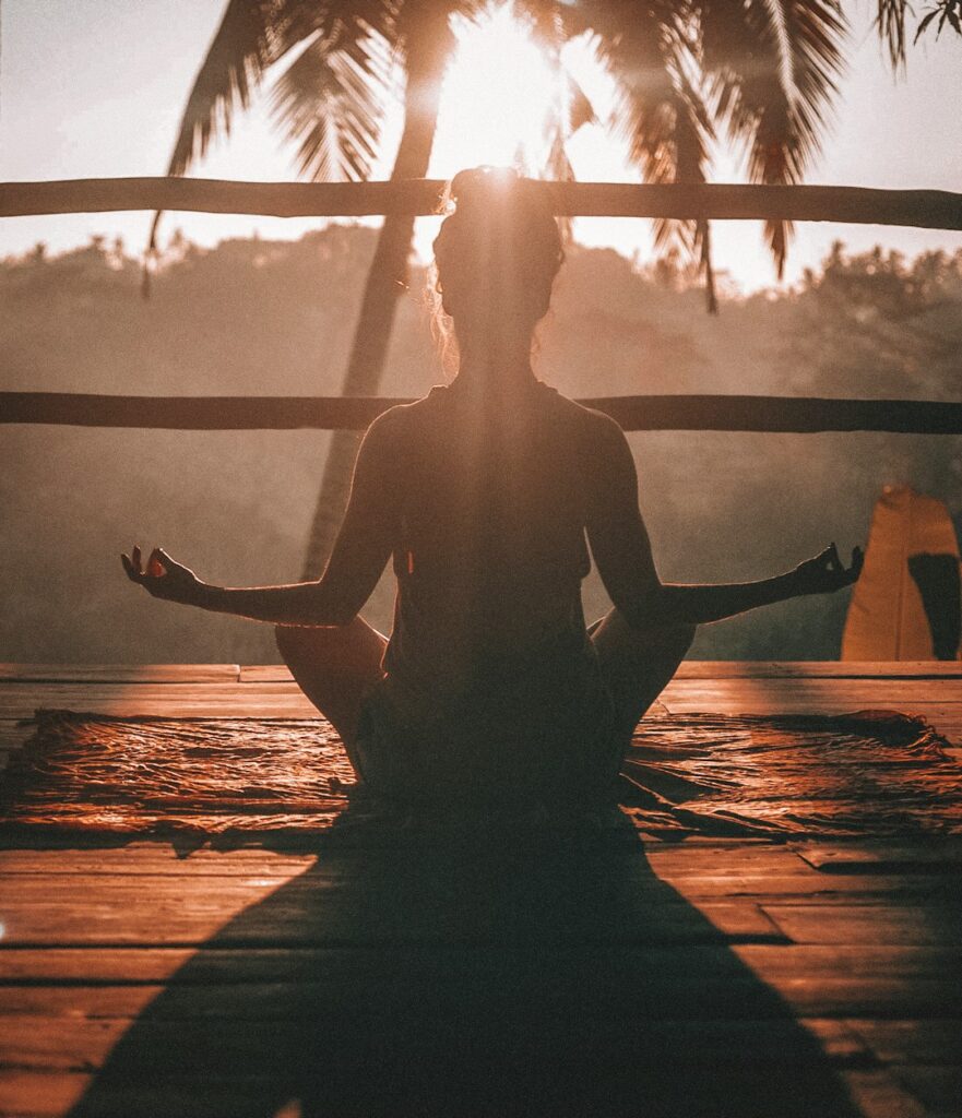 Silhouette of a person meditating in front of a sunset window with palm trees