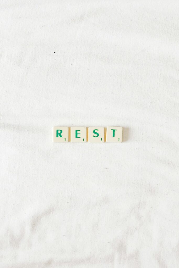 Scrabble tiles spelling the word REST on white bed linen