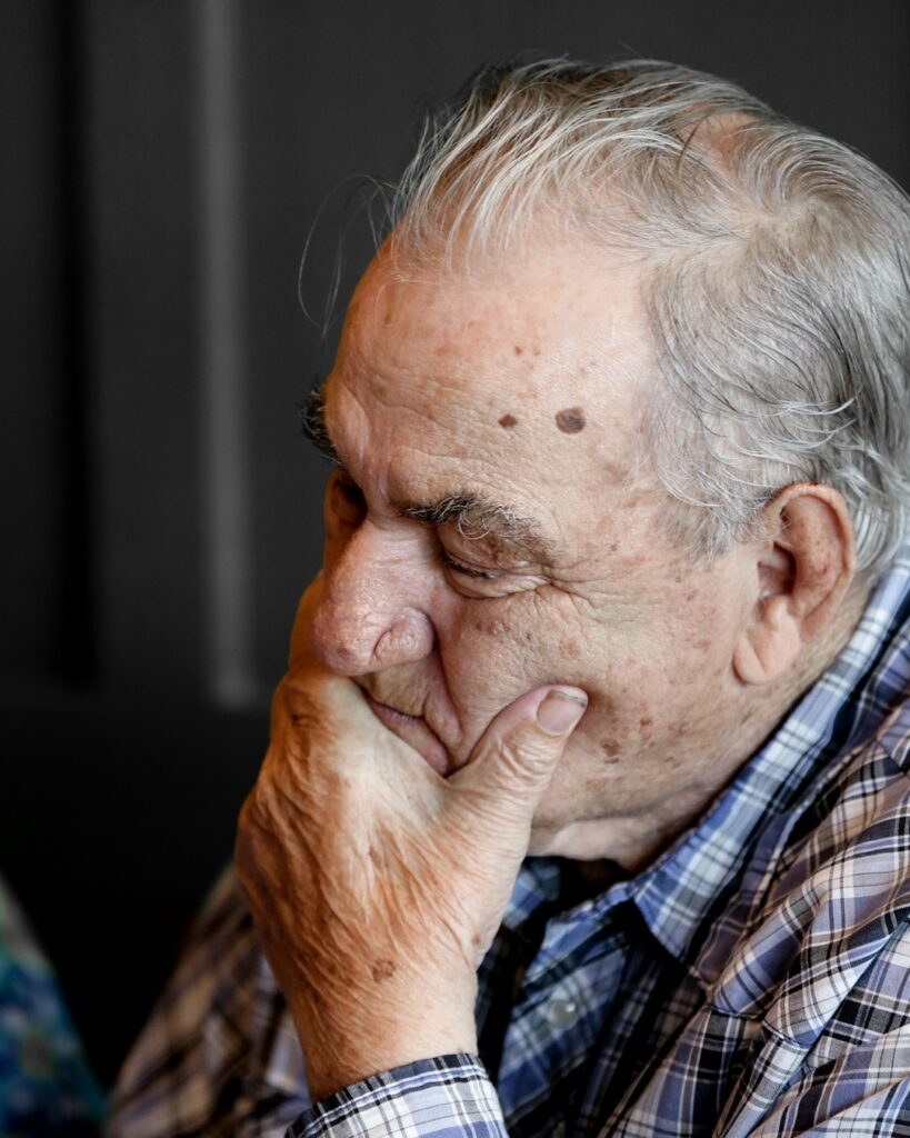 Older man with his hand over his mouth and his eyes closed, looking worried