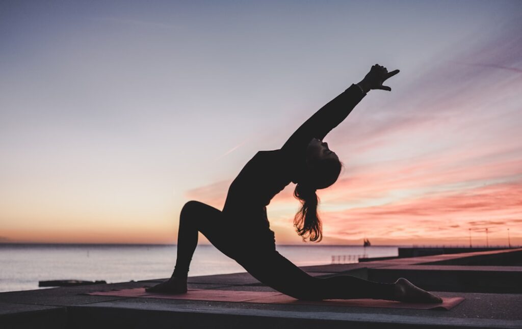 Silhouette of a woman doing a yoga stretch on a beach at sunset